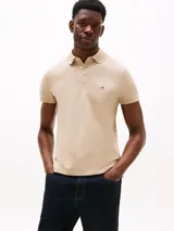 Chomba de mangas cortas color beige, corte slim, con cuello polo y cartera de dos botones. Logo de Tommy Hilfiger bordado en el pecho.