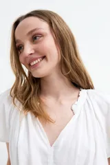 Blusa de manga corta color negro, con escote en V y frunces en los hombros, de diseño holgado y ligero.