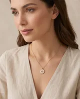 Collar de acero con baño de oro, compuesto por una cadena fina y un dije circular con incrustaciones de nácar y circonias.