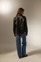 Sobrecamisa de cuero sintético en color negro, con cuello clásico, cierre frontal mediante botones metálicos y dos bolsillos frontales con solapa. Presenta costuras a la vista y mangas largas con puños abotonados.