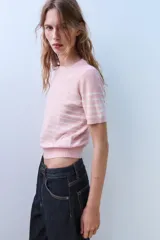 Top de punto de manga corta y cuello redondo, de color rosado con rayas horizontales blancas y aplicación de lentejuelas brillantes en toda la prenda.