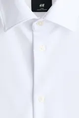 Camisa H&M de corte slim fit, color blanco, confeccionada en tejido elástico con cuello italiano y cierre frontal de botones.