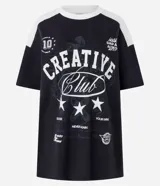 Remera oversized negra con mangas y cuello blanco, con estampado frontal que incluye la frase "Creative Club" en blanco, estrellas y otros gráficos en estilo vintage.