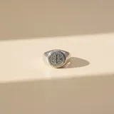 Anillo tipo sello de plata 925 con diseño circular grabado de la medalla de San Benito en la parte superior.