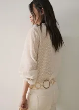 Blusa de tejido fluido color crudo, con escote en V, mangas largas y volantes decorativos en el frente y cuello.