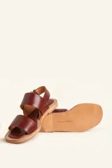 Sandalias planas de cuero negro con tiras anchas en el empeine y cierre ajustable con hebilla metálica en el talón.