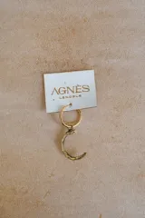 Arete tipo argolla dorada con un dije colgante en forma de media luna o letra 'C' con textura rugosa y acabado envejecido/bronce. Se vende por unidad.
