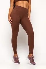 Calza deportiva de tiro alto color marrón, confeccionada en tejido técnico de alto rendimiento con compresión. Presenta bolsillos laterales funcionales y detalles reflectivos para mayor visibilidad.