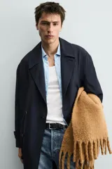 Trench de corte relajado confeccionado en tejido con viscosa, de color azul marino. Presenta cuello con solapas de muesca, cierre frontal de botonadura cruzada, mangas largas con puños ajustables mediante trabillas y bolsillos de vivo en la cadera. Incluye una abertura central en la espalda.