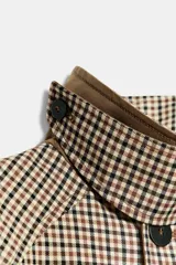 Trench de corte recto con estampado de cuadros, cuello alto con trabilla y cierre frontal de botones. Presenta mangas largas, bolsillos laterales y abertura en la espalda.