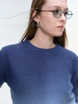 Buzo tejido de punto con diseño degradé que transiciona de azul oscuro a celeste claro. Presenta cuello redondo, mangas largas y puños acanalados, con un corte holgado y relajado.