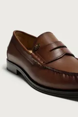 Mocasín de vestir de cuero color marrón, con diseño tipo antifaz en el empeine, costuras visibles en la puntera y suela a contraste.