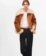 Chaqueta estilo aviador de ante sintético en color marrón con detalles de borrego sintético en el cuello, los puños, la solapa y el dobladillo inferior, con bolsillos laterales y cierre frontal con cremallera.