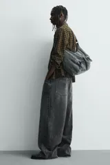 Bolso tipo bandolera confeccionado en tejido denim de algodón con efecto lavado. Cuenta con un compartimento principal con cierre de cremallera, un bolsillo interior con cierre y dos bolsillos frontales, uno con cierre de cremallera y otro con cierre de fruncido. Incluye asa de hombro ajustable.