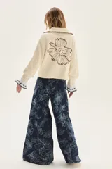 Cardigan de punto color crudo con textura, cuello camisero con borde en contraste, mangas largas con puños acampanados y detalle de bordado floral en la espalda.