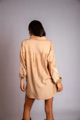 Camisa beige de corte amplio, con cuello clásico, cierre frontal con botones, mangas largas con puños abotonados y bordado floral en las mangas.