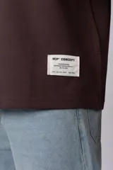Remera de corte oversize color beige, con cuello redondo y etiqueta decorativa pequeña en el ruedo inferior.
