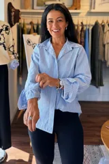 Camisa de corte clásico con estampado de rayas verticales en tonos celeste y blanco. Presenta cuello camisero, cierre frontal de botones y mangas largas con puños con volados.
