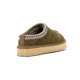 Pantufla tipo zueco de cuero gamuzado color verde oliva, con interior de peluche y suela de plataforma de goma color beige. Presenta un detalle de costura decorativa trenzada en el borde superior.