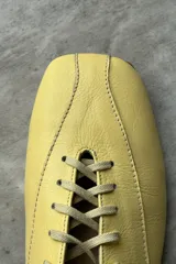 Zapato tipo flat de cuero amarillo con cordones frontales y punta cuadrada.