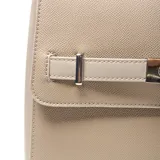 Mochila de diseño estructurado en color taupe, confeccionada en material símil cuero con textura granulada. Presenta una solapa frontal con cierre metálico tipo torniquete y una correa decorativa horizontal. Incluye asa superior y logo de la marca grabado en la parte inferior.