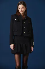 Saco corto color bordó con cuello mao, cierre frontal de botones dorados y cuatro bolsillos delanteros con solapa y botón dorado. Presenta un parche decorativo en la manga izquierda.