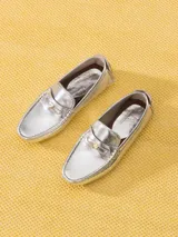 Mocasín de cuero vacuno con acabado metalizado plateado y textura tipo crocco. Presenta un aplique metálico en forma de corazón sobre el frente y suela de goma con tacos.