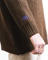 Buzo unisex de tejido de punto grueso en lana merino, color rojo, con cuello redondo y diseño de calce relajado. Presenta un detalle bordado a mano en contraste en la manga.