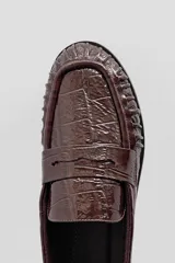 Mocasín de cuero marrón con textura croco y acabado brillante, de diseño clásico con detalle de antifaz en el empeine y costuras pespunteadas alrededor de la puntera.