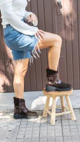 Botas de caña media combinadas en gamuza y cuero vacuno color marrón oscuro. Presentan un diseño con tiras decorativas cruzadas sobre el empeine con hebillas metálicas, cierre lateral y suela de goma con plataforma dentada.