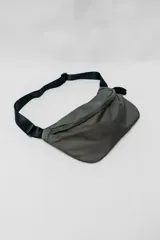 Bandolera de diseño minimalista en color verde oliva, con correa ajustable de cinta negra y cierre superior.