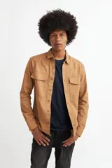 Camisa marrón de manga larga con cuello clásico, cierre frontal con botones, dos bolsillos con solapa abotonada en el pecho y puños abotonados.