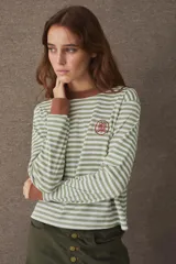 Remera de manga larga con diseño de rayas horizontales en color verde y blanco. Presenta cuello redondo y puños en color marrón a contratono, con un pequeño escudo bordado en el pecho.