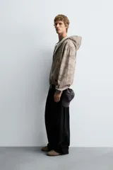 Cazadora negra de algodón con efecto lavado, corte relajado y capucha ajustable. Presenta cierre frontal de cremallera, bolsillos frontales tipo canguro y elásticos en puños y bajo.