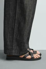 Sandalia plana negra con tiras anchas cruzadas sobre el empeine y una tira que separa el dedo gordo. Posee plantilla anatómica.