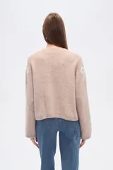 Cárdigan color beige con estampado de moños blancos, escote en V y cierre frontal con botones.