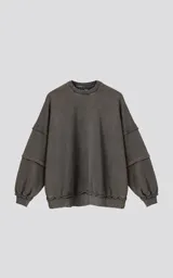 Buzo de cuello redondo, color gris oscuro con efecto desgastado (acid wash). Presenta costuras expuestas y detalles de roturas en los bordes. El calce es oversize y crop, con mangas largas abullonadas y puños y ruedo con terminación deshilachada y ondulada.