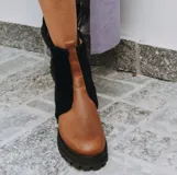 Botas de cuero marrón con la caña recubierta de corderito verde. Presentan una suela de plataforma tipo track en color beige y un tirador en la parte posterior para facilitar el calce.