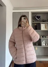 Campera puffer acolchada de color rosado, con cierre frontal completo, cuello alto y bolsillos laterales.
