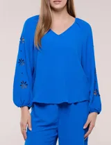 Blusa azul de corte holgado y fluido, con escote en V y mangas largas raglán que presentan detalles de calados con forma de flores y puños elastizados.