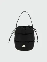 Cartera tipo bucket Moncler modelo Caradoc, de diseño acolchado y color negro, con cierre superior fruncido mediante cordón ajustable, asa superior de hombro y detalle del logo metálico de la marca en el frente.