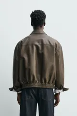 Cazadora tipo bomber de corte relajado confeccionada en tejido efecto piel color verde oscuro. Presenta cuello solapa, cierre frontal con cremallera, bolsillos de plastrón con solapa en el pecho, bolsillos ocultos en la cadera y bajo con elástico.