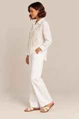 Camisa blanca de manga larga confeccionada en lino y viscosa, con cuello camisero, cierre frontal con botones y delicados bordados florales con apliques de perlas y pedrería en el frente.