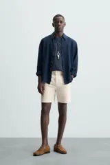 Bermuda de hombre color beige claro, corte regular fit, con pliegues frontales, bolsillos delanteros y bolsillos traseros de doble vivo con botón.