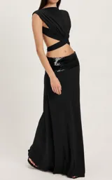 Conjunto de dos piezas negro compuesto por un top cruzado asimétrico sin mangas con espalda descubierta y una pollera larga de corte recto con pretina ancha de lentejuelas brillantes.