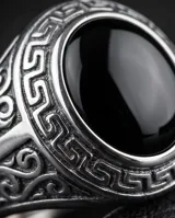 Anillo de acero tipo sello con piedra central redonda color negro y detalles de guarda griega en los laterales.