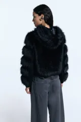 Campera de pelo ecológico negro con recortes en denim negro. Presenta cierre metálico frontal, alamares metálicos decorativos, capucha y bolsillos laterales. Las mangas tienen un diseño con recortes que alternan pelo y denim, y cuenta con elástico en la cintura.