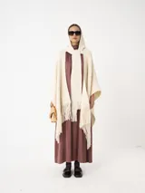 Ruana color crudo de tejido de punto grueso con capucha y bufanda integrada. Presenta flecos en el borde inferior.