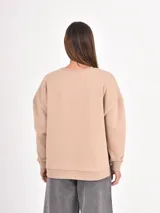 Buzo de cuello redondo, manga larga con puños elásticos y diseño holgado. Presenta un corte asimétrico con aberturas laterales en el ruedo.