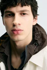 Cazadora de hombre, corte relaxed fit, color blanco hueso o crema, con acabado brillante. Presenta cuello solapa, manga larga, dos bolsillos de plastrón con solapa en la cadera y cierre frontal con botones a presión ocultos por una solapa.